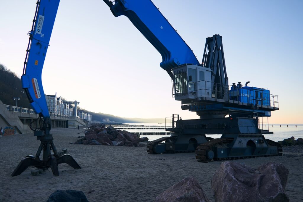 Blue industrial crane on a sandy beach near ocean