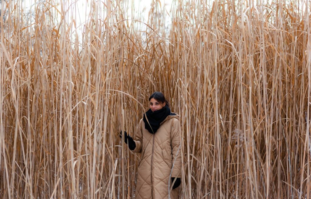 man in beige jacket and black pants wearing black cap standing on brown grass field during